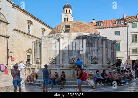 Dubrovnik. Croazia - 2 dicembre 2025: Turisti e visitatori riposano e bevono acqua presso la grande Fontana di Onofrio, un famoso monumento storico nel Foto Stock