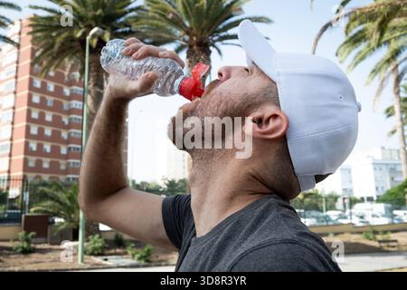 Il giovane beve acqua dopo un allenamento all'aperto in città. Foto Stock