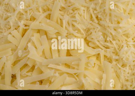 formaggio giallo grattugiato finemente su una grattugia per pizza o pasta, formaggio grattugiato giallo con pezzi per cucinare vari alimenti Foto Stock
