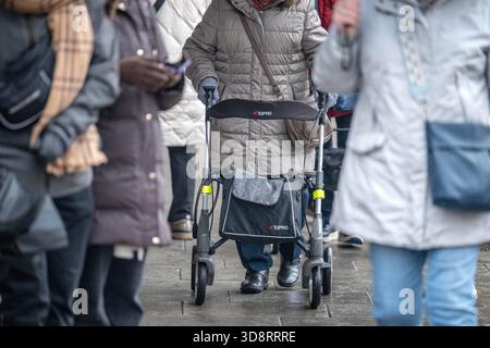 2 dicembre 2025, Brema: Una persona anziana con un telaio che cammina attraverso una zona pedonale trafficata. Venerdì, il Bundestag deciderà la riforma pensionistica prevista, che prevede un livello pensionistico stabile, periodi prolungati di crescita dei figli, possibilità di reddito supplementare esentasse in età avanzata e altre modifiche alle pensioni di vecchiaia. Foto: Sina Schuldt/dpa Foto Stock
