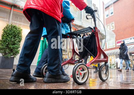 2 dicembre 2025, Brema: Una persona anziana con una cornice rossa che cammina attraverso una trafficata strada dello shopping sotto la pioggia. Venerdì, il Bundestag deciderà la riforma pensionistica prevista, che prevede un livello pensionistico stabile, periodi prolungati di crescita dei figli, possibilità di reddito supplementare esentasse in età avanzata e altre modifiche alle pensioni di vecchiaia. Foto: Sina Schuldt/dpa Foto Stock