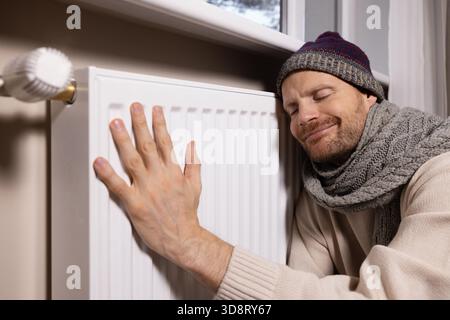 uomo felice che si riscalda davanti al radiatore nella stanza fredda di casa quando la stagione di riscaldamento è finalmente iniziata Foto Stock