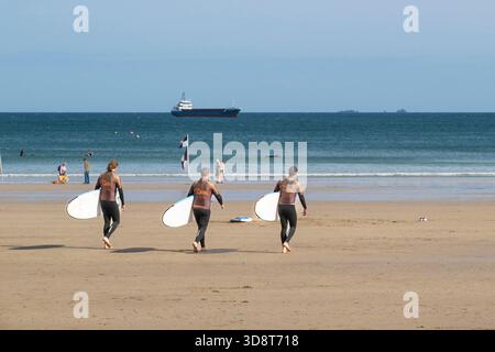 Tre vacanzieri in una lezione di surf con la Cornish Wave Surf School presso Towan Beach a Newquay, in Cornovaglia, in Inghilterra, nel Regno Unito. Foto Stock