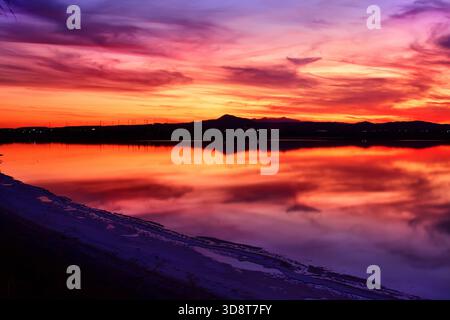 Crepuscolo al lago salato di Larnaca, Cipro, con colori arancioni, blu e viola che si riflettono sull'acqua calmo sotto un cielo nuvoloso. Foto Stock