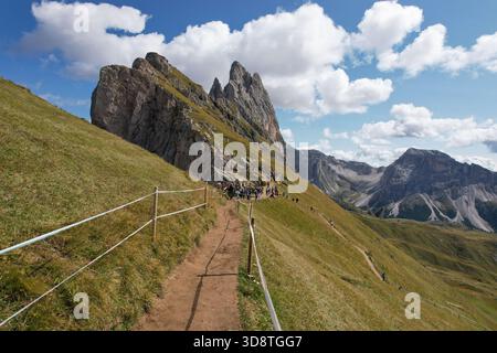 Vista di un sentiero tortuoso attraverso un paesaggio verdeggiante che conduce verso aspre vette sotto un cielo adornato da soffici nuvole, Ortisei, Trentino-alto Adige Foto Stock