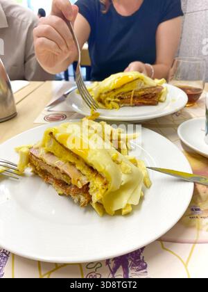 Francesinha, un sandwich a strati di specialità portoghesi con uova fritte, formaggio e prosciutto su un piatto bianco con patatine fritte, che mostra un delizioso piatto Foto Stock