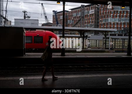 Persona che cammina sul binario della stazione ferroviaria di Tolosa-Matabiau con un treno rosso e edifici moderni sullo sfondo a Tolosa in alta Garonna Foto Stock