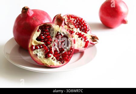 Frutta fresca di melograno e semi di melograno in un piatto su sfondo bianco. Cibo sano. Primo piano. Foto Stock