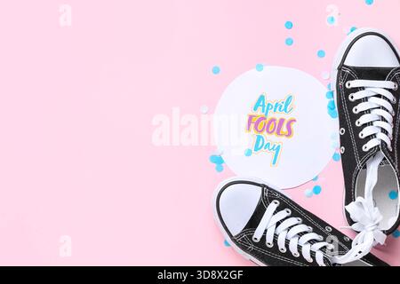 Scarpe con lacci legati, cartolina natalizia e coriandoli su sfondo rosa. Festa del Fools Day di aprile Foto Stock