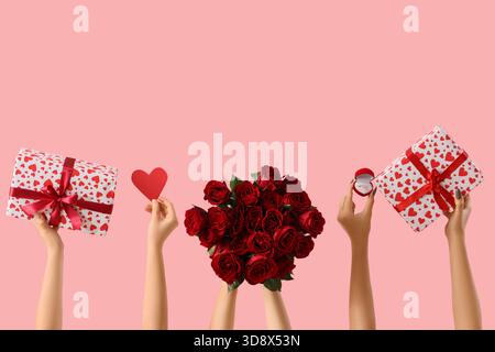 Mani femminili con rose, scatole regalo e anello di innesto su sfondo rosa. Festa di San Valentino Foto Stock
