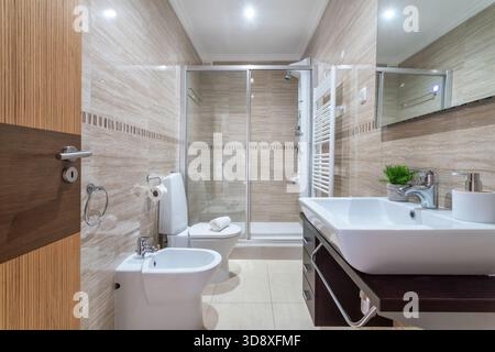 Un bagno elegante con doccia in vetro, lavandino moderno e piastrelle eleganti. L'illuminazione soffusa crea un'atmosfera rilassante in questo spazio ben progettato Foto Stock