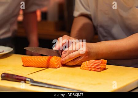 Lo chef affetta sapientemente filetti di salmone fresco su un tagliere di legno in una cucina professionale, dimostrando competenza culinaria e precisione. Foto Stock