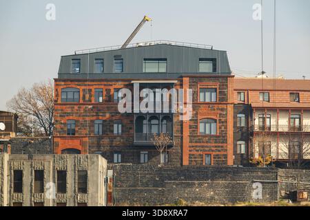 Erevan Armenia 10.25.2025. Un grande edificio in mattoni con un balcone e una gru in cima. L'edificio è circondato da altri edifici e da una recinzione Foto Stock