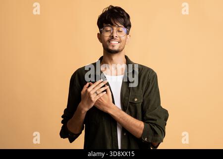 Giovane sorridente con gli occhiali che indossa una camicia verde su sfondo arancione chiaro Foto Stock