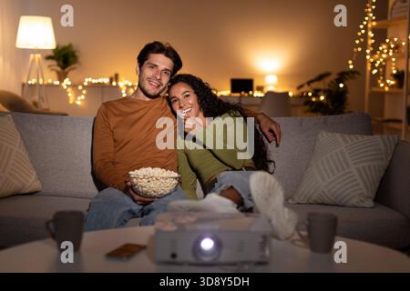 La coppia felice si diverte a guardare film a casa con proiettore e popcorn Foto Stock