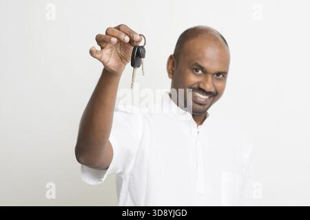 Un agente immobiliare o un venditore indiano maturo che mostra un uomo d'affari uomo d'affari indiano chiave, in piedi su un semplice sfondo con l'ombra Foto Stock