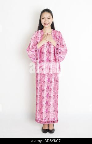 Ritratto di una giovane donna del sud-est asiatico in un tradizionale abito batik malese, in piedi su uno sfondo semplice Foto Stock
