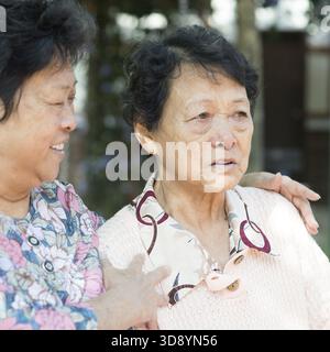 Donna asiatica matura consolando la sua vecchia madre piangente al parco verde naturale all'aperto Foto Stock
