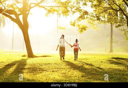 Vista posteriore della madre asiatica tenendo la figlia della mano a correre verso la luce Foto Stock