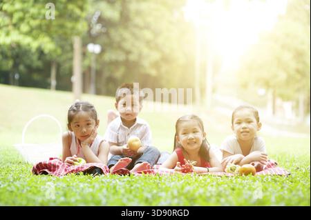 Ritratto di picnic per bambini asiatici al parco, sdraiati sul prato. I bambini si divertono all'aperto. Sfondo luminoso del sole mattutino Foto Stock