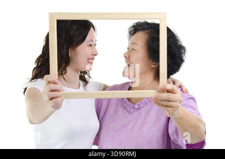 Ritratto di mani anziane asiatiche e di figlie adulte che tengono una cornice fotografica vuota, che si guardano l'un l'altra, isolata su sfondo bianco Foto Stock