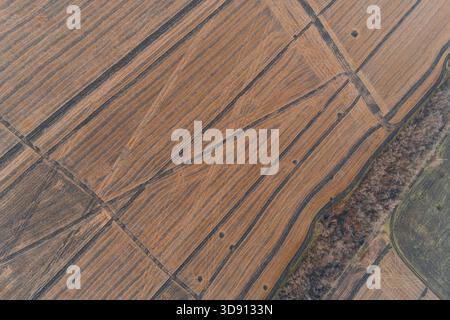 Ripresa astratta di droni che cattura intricati pattern lineari e geometrici di un campo appena coltivato. La consistenza calda del terreno è leggermente disturbata da piccole tracce di esplosione sparse, creando uno sfondo unico. Foto Stock