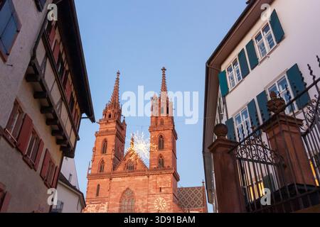 BASILEA, SVIZZERA - 16 DICEMBRE 2024: Le torri gemelle della storica cattedrale di Basilea Minster (Munster) illuminate al crepuscolo con un Natale sospeso Foto Stock