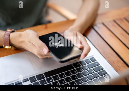 Chiang mai, Tailandia - 8 maggio 2025: Primo piano di un uomo che tiene le mani con lo smartphone utilizzando l'applicazione X (precedentemente Twitter) sopra il laptop su un tavolo di legno. Foto Stock