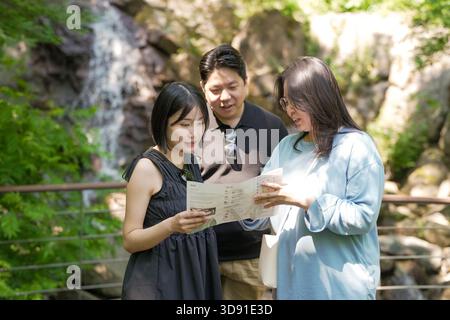 Tre persone sono in piedi vicino a una cascata, guardando una mappa. La donna in mezzo sta leggendo la mappa mentre l'uomo e la donna a destra sono a guardare Foto Stock