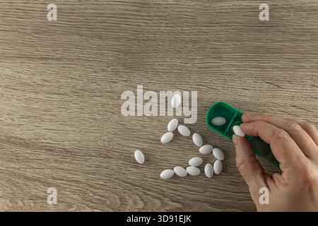 L'uomo dipendente da farmaci da prescrizione mette pillole in una scatola di medicinali, pillole bianche sparse su un tavolo di legno Foto Stock
