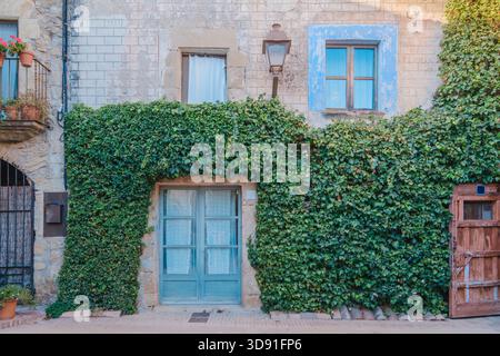Porta doppia di colore blu vibrante posta in una porta rustica in pietra ad arco, con una sedia in vimini e tavolo su una terrazza esterna in legno Foto Stock