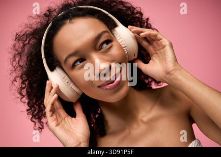 Una giovane donna felice ama i suoi brani preferiti con le cuffie su sfondo rosa. Foto Stock