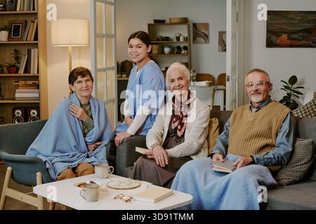 Ritratto di una giovane donna ispanica che assiste tre anziani che si rilassano all'interno Foto Stock