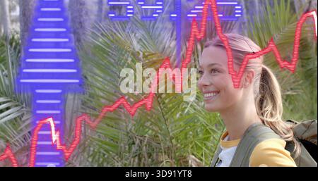 Donna sorridente in piedi nel parco tra le palme, con la parte superiore gialla e il branco, sovrapposizioni rosso-blu, spazio copia Foto Stock