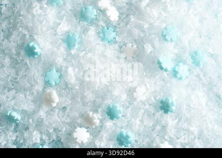 Foto macro di texture bianca innevata decorata con piccoli fiocchi di neve blu a forma di stella. Foto Stock