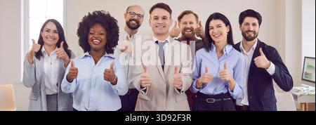Ritratto del team aziendale multinazionale che mostra le pollice in ufficio Foto Stock