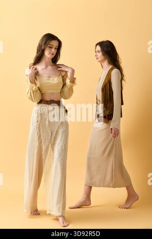 Due giovani gemelle presentano abiti eleganti su uno sfondo giallo brillante. Foto Stock