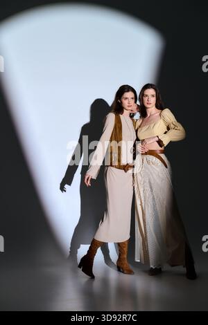 Due giovani splendide sorelle gemelle mettono in mostra il loro abbigliamento elegante su uno sfondo ombreggiato. Foto Stock