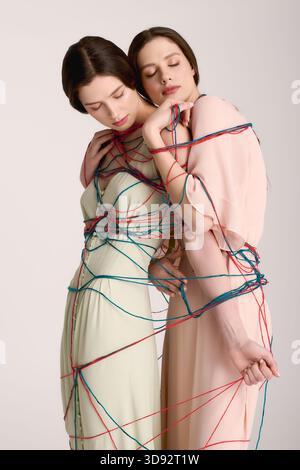 Due bellissime gemelle presentano abiti eleganti e divertenti avvolti in fili colorati. Foto Stock