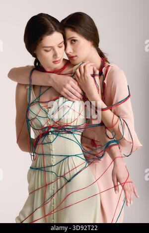Le giovani e splendide sorelle gemelle sfoggiano il loro stile unico, intrecciate in vivaci fili. Foto Stock