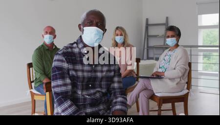 Uomo maturo seduto con camicia scura a quadri e maschera chirurgica nella sala riunioni, appunti senior Foto Stock