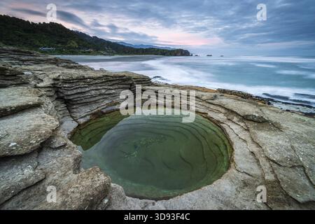 Piscina circolare di pietra calcarea a strati sulla costa a Punakaiki nel Parco Nazionale di Paparoa, costa occidentale, Isola del Sud, nuova Zelanda. Autunno (maggio) 2025. Foto Stock