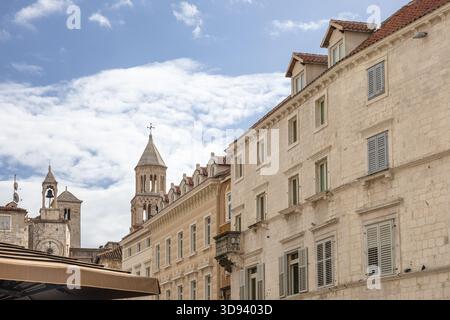 Un paesaggio urbano europeo illuminato dal sole caratterizzato da edifici in pietra intemprata, un orologio e un campanile di primo piano, e terrazze sul tetto con ombrelloni, che evocano il vecchio stile Foto Stock