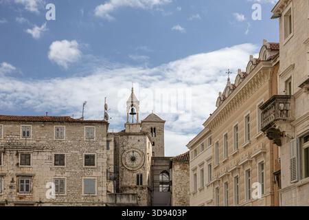 Un paesaggio urbano europeo illuminato dal sole caratterizzato da edifici in pietra intemprata, un orologio e un campanile di primo piano, e terrazze sul tetto con ombrelloni, che evocano il vecchio stile Foto Stock