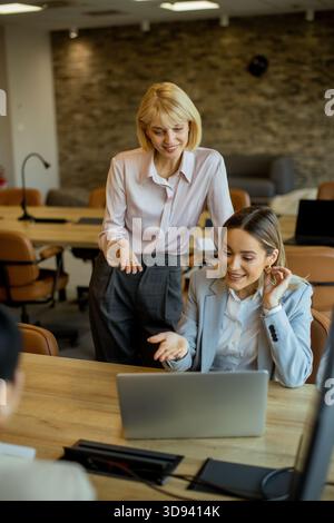 In un ufficio contemporaneo, due donne si impegnano in una discussione su un progetto durante la revisione di un notebook. L'atmosfera è collaborativa, piena di natu Foto Stock