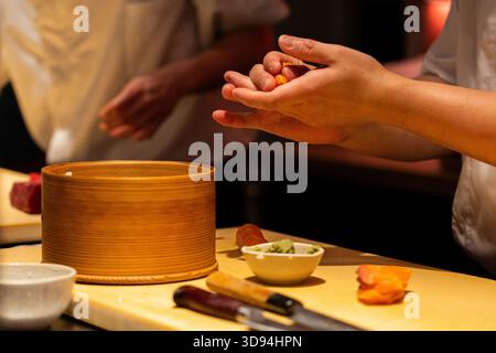 Lo chef esperto prepara sushi con ingredienti freschi, mostrando tecniche culinarie e colori vivaci in un ambiente moderno. Foto Stock