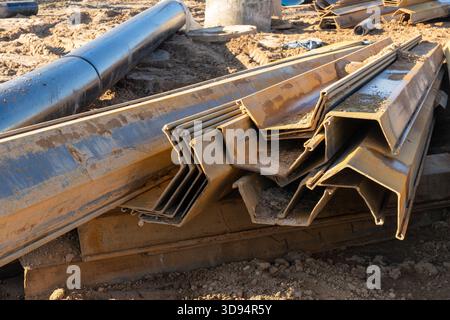 Uno scatto ravvicinato di diversi pali di lamiera d'acciaio incastrati, comunemente noti come pali di lastre di Larssen, in un soleggiato cantiere all'aperto in mezzo ad altri metri Foto Stock