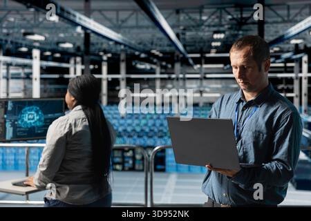Team di server farm composto da tecnici che utilizzano i dispositivi per automatizzare l'infrastruttura, eseguendo test del software di intelligenza artificiale. Programmatore di data center e collega che regolano i modelli di deep learning Foto Stock