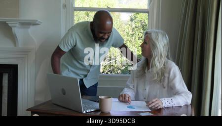 Uomo in camicia a manica corta che si appoggia, donna in camicetta che tiene a casa il grafico a torta, con notebook Foto Stock
