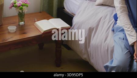 Donna seduta con top bianco, gonna blu sul letto destro, comodino con vaso o libro o occhiali, copia Foto Stock